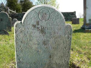 Arch-shaped slate stone flanked by two smaller arches from which foliate designs descend. An oval face over wings is carved on center arch.