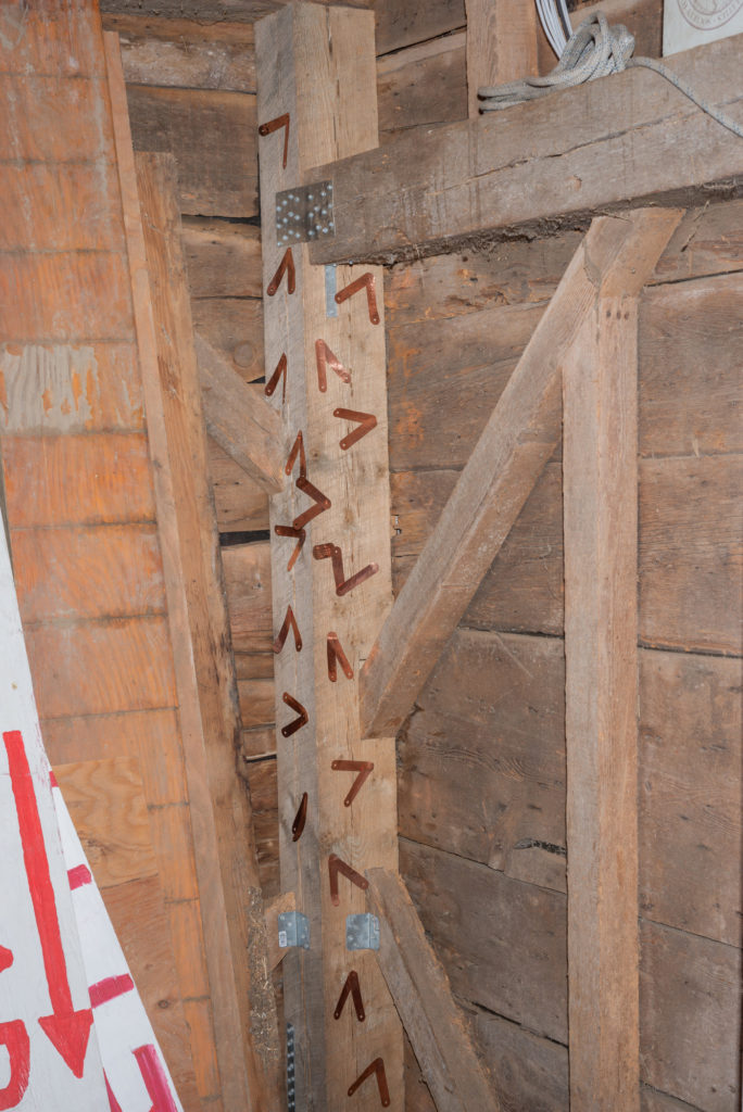 Inside a wood-framed barn, the new corner post is festooned with copper tags.