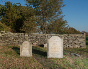 Two light gray granite headstones inside a stone wall