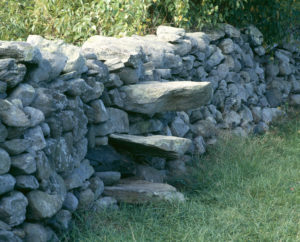 Stone wall in the grass with three projecting stone steps cantilevered out