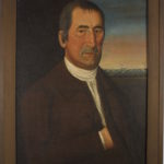 Oil painting of a white man with short dark hair and a brown suit. In the background is a ship at sea and a lighthouse.