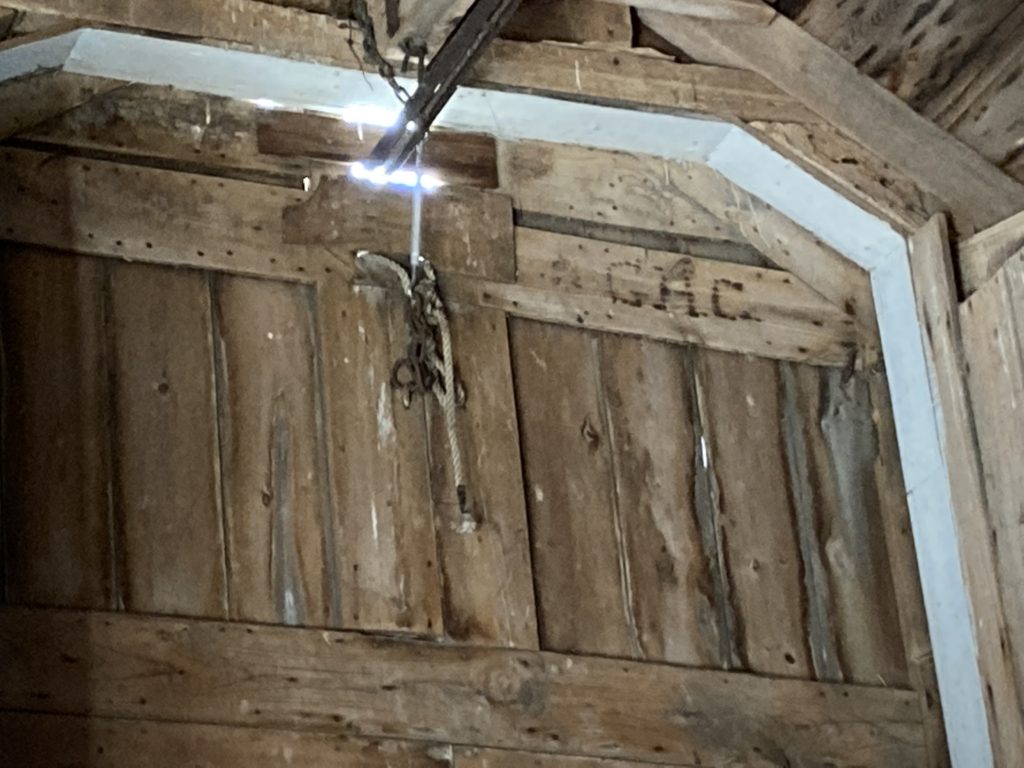 A wood paneled door with clipped top corners and a metal beam with rope above it