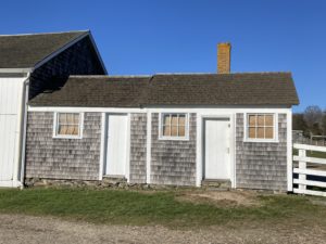 two small shingled buildings with white trim are attached to each other and a larger white barn