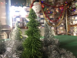 Tinsel garland, colored lights, and a snowman decorate a small room with shelves of organized boxes