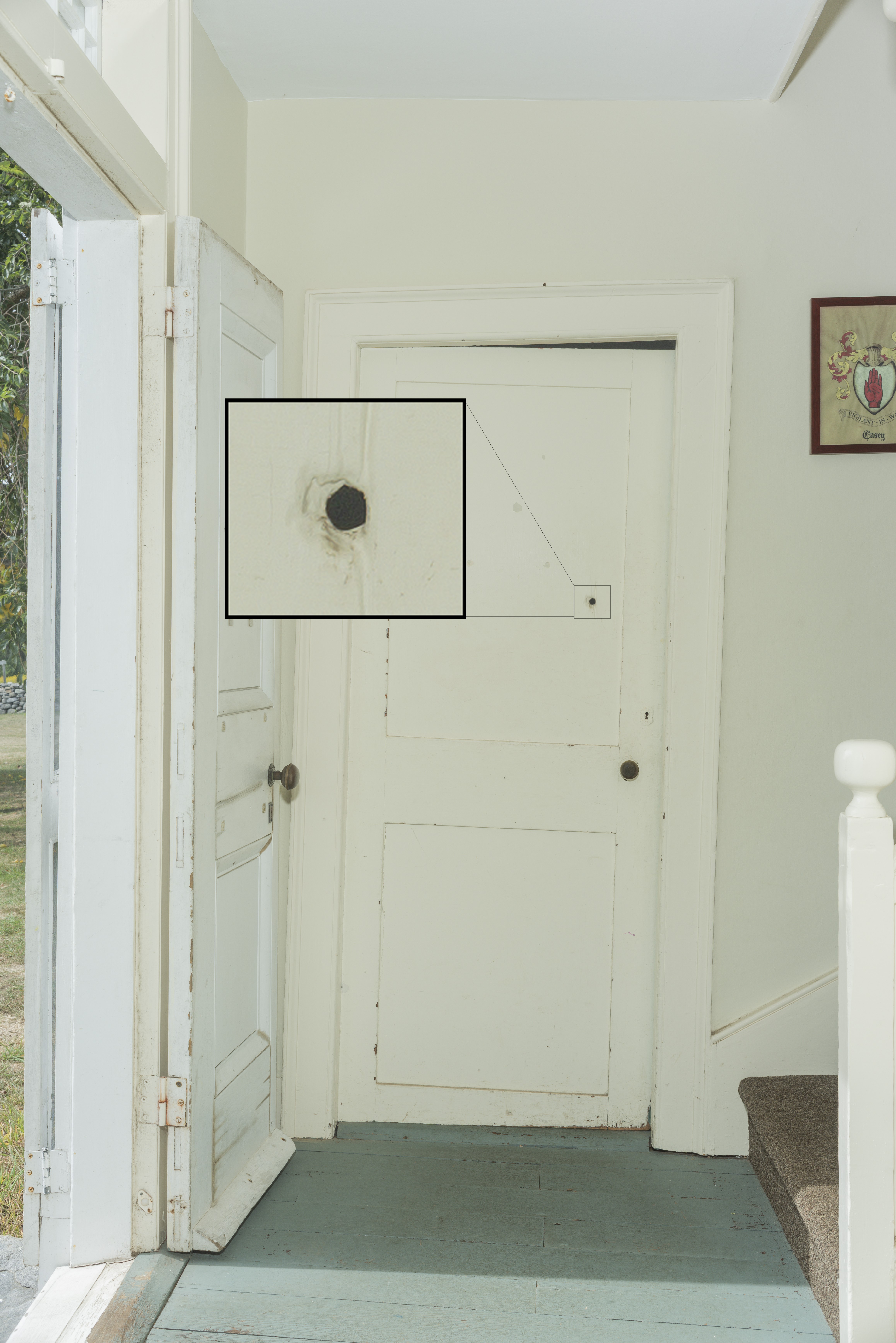 In a white-painted hall with a paneled door, a half-inch hole in the door is enlarged in a graphic.