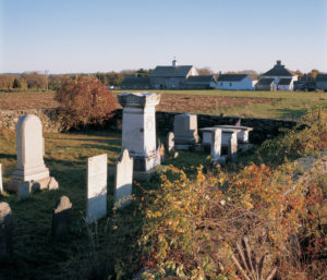 Cemetery stones in the foreground with farm buildings in the background