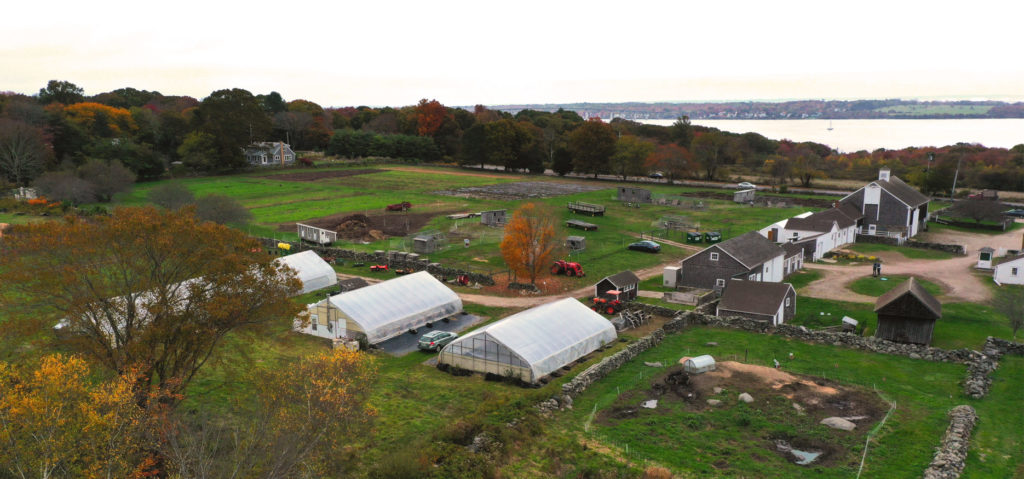 overhead view of farm with three greenhouses, green fields, and several outbuildings 